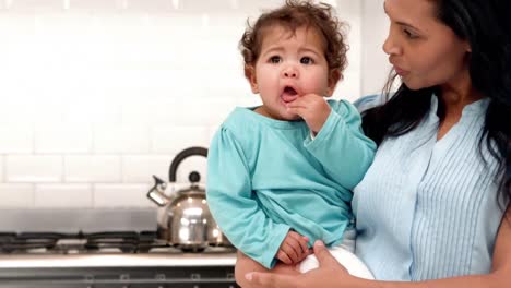 -Smiling-mother-carrying-baby-boy-in-kitchen-