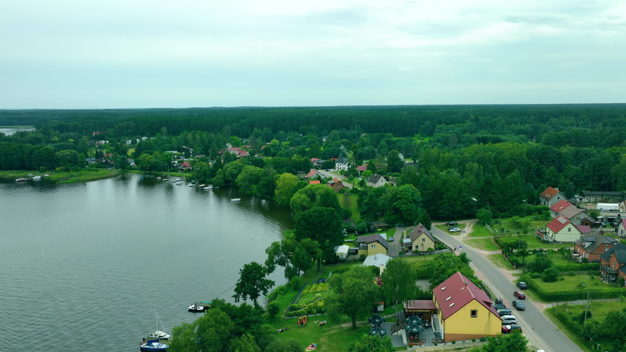 Aerial shot of a small lakeside village surrounded by lush forests and tranquil waters of Jeziorak lake, with homes nestled close to the shoreline, perfect for serene countryside scenes