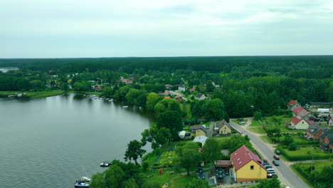aerial shot of a small lakeside village surrounded by lush forests and tranquil waters of jeziorak lake, with homes nestled close to the shoreline, perfect for serene countryside scenes