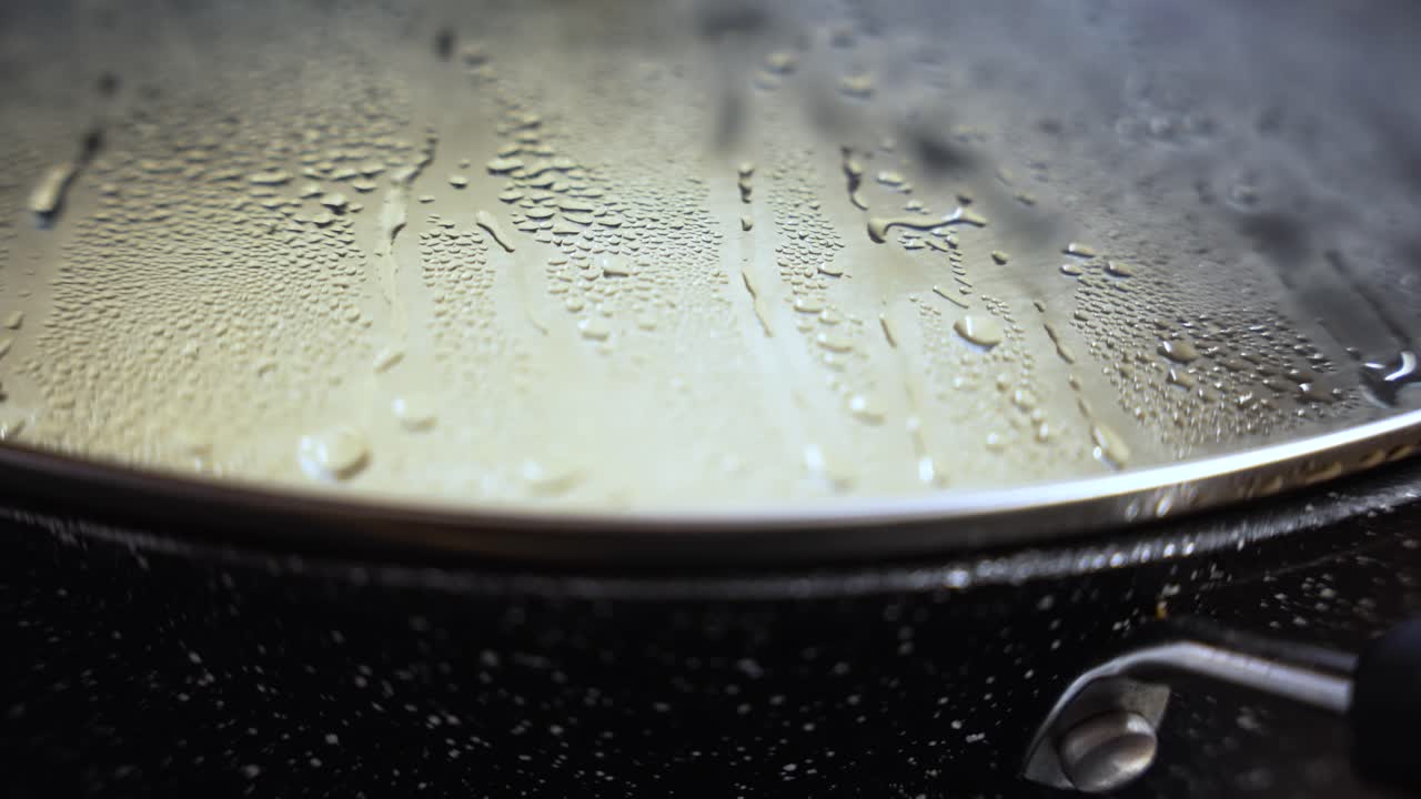 Close up of steam droplets forming on the inside of a metal pan lid, indicating ongoing cooking process and heat
