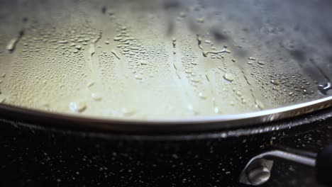 close up of steam droplets forming on the inside of a metal pan lid, indicating ongoing cooking process and heat