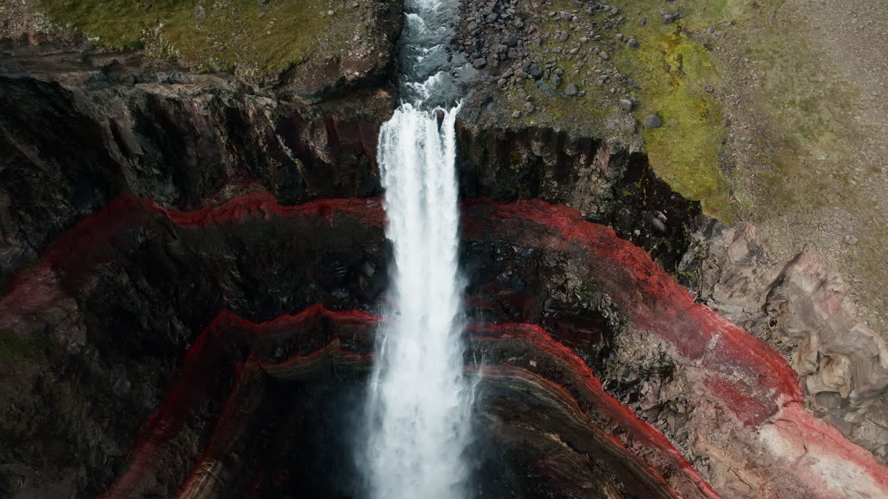 Close up aerial drone shot of Hengifoss Waterfall in motion, Iceland, sunny day, green grass, red clay. Part 5.