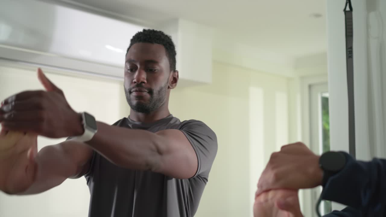 Diverse male workout partners warming up wrists in home studio after adjusting smartwatch strap