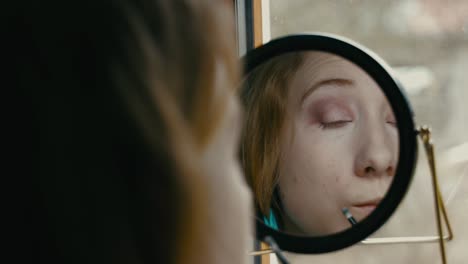woman applying eye makeup in front of a mirror