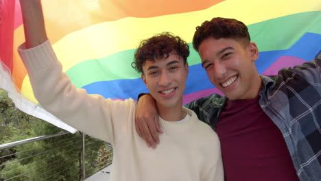 smiling multiracial gay couple holding rainbow flag and embracing, celebrating lgbtq+ pride, at home