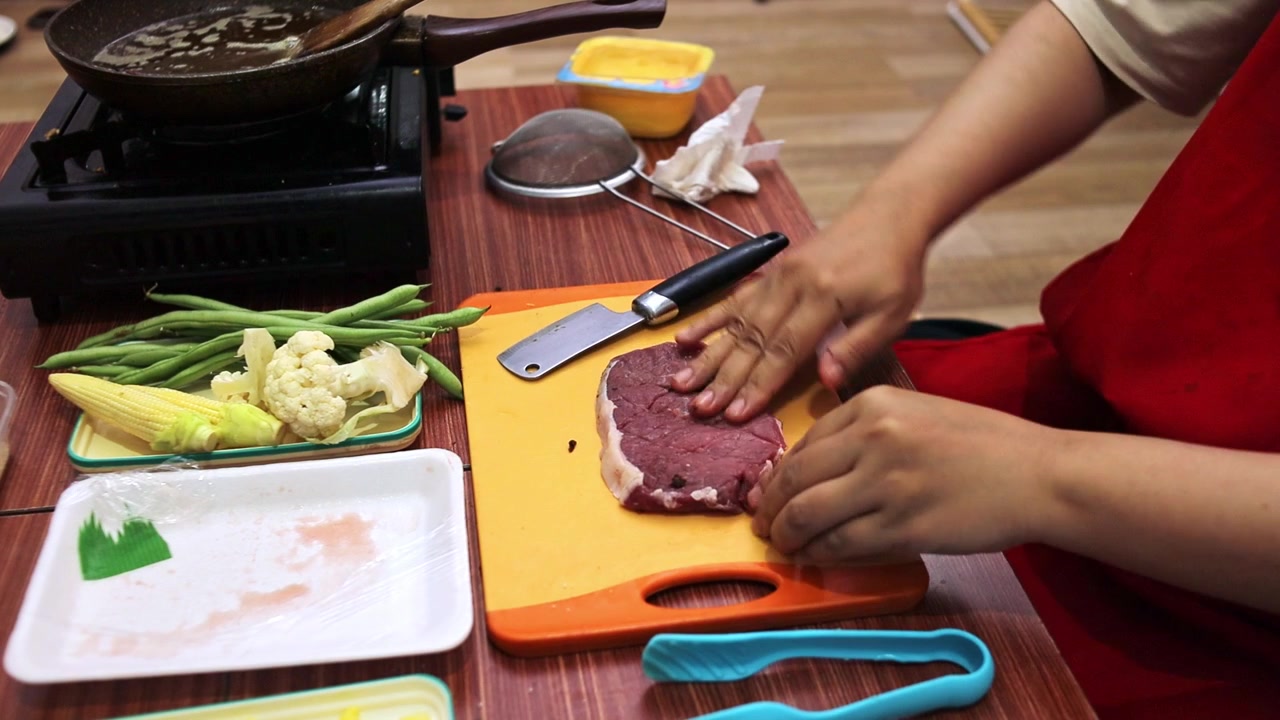 Un cuoco casalingo condisce e preme le spezie su entrambi i lati di una bistecca cruda su un tagliere.