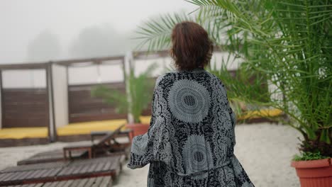 back view of a barefoot woman in a graceful peignoir running by resort beach on a summer day