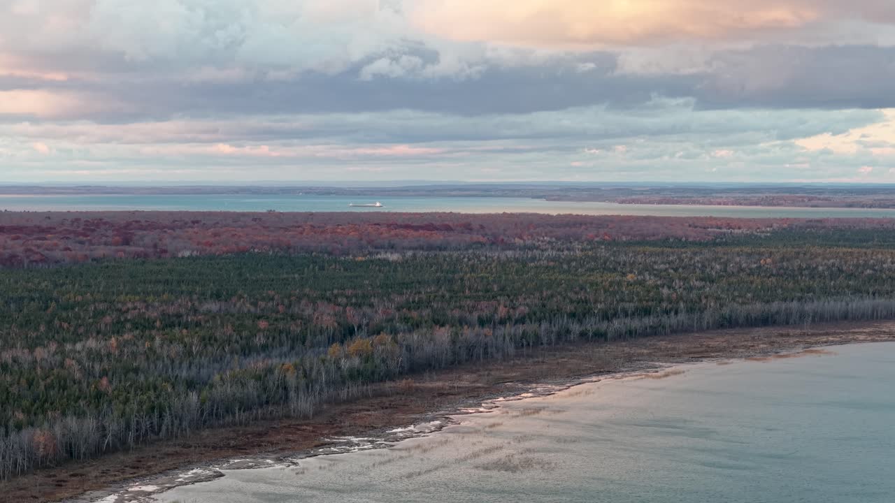 Aerial drone shot of Lake Superior’s shoreline at dusk, with moody skies and a dense forest meeting calm, reflective waters