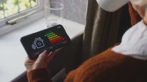 senior woman using app to measure energy efficiency standing by radiator at home