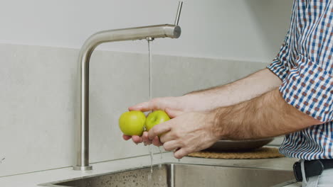 cerca de las manos del hombre lavando dos manzanas verdes en un fregadero de cocina moderno