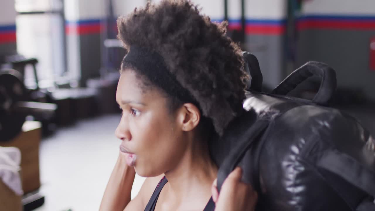 Video of determined african american woman working out with weights at a gym