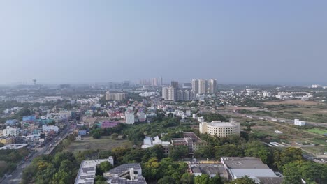 an aerial view of an indian city, hazy daytime, overlooking a sprawling urban and suburban landscape. there is a mix of low-rise residential and commercial buildings with varied roof colors