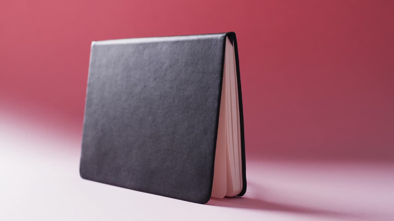 Close up of open black book standing horizontal with copy space on red background in slow motion
