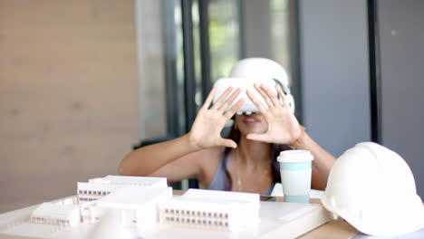 using vr headset, woman exploring architectural model with coffee cup on table