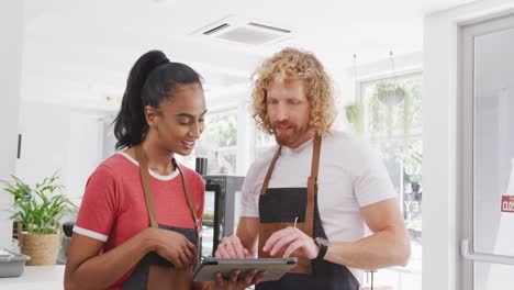 Felices-Y-Diversos-Baristas-Masculinos-Y-Femeninos-Usando-Tableta-Y-Hablando-En-Su-Café