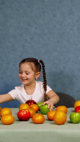 cheerful little girl playing with ripe fruits on the table. happy child building a tower with fresh organic apples. healthy fruits full of vitamins on the table. vertical video
