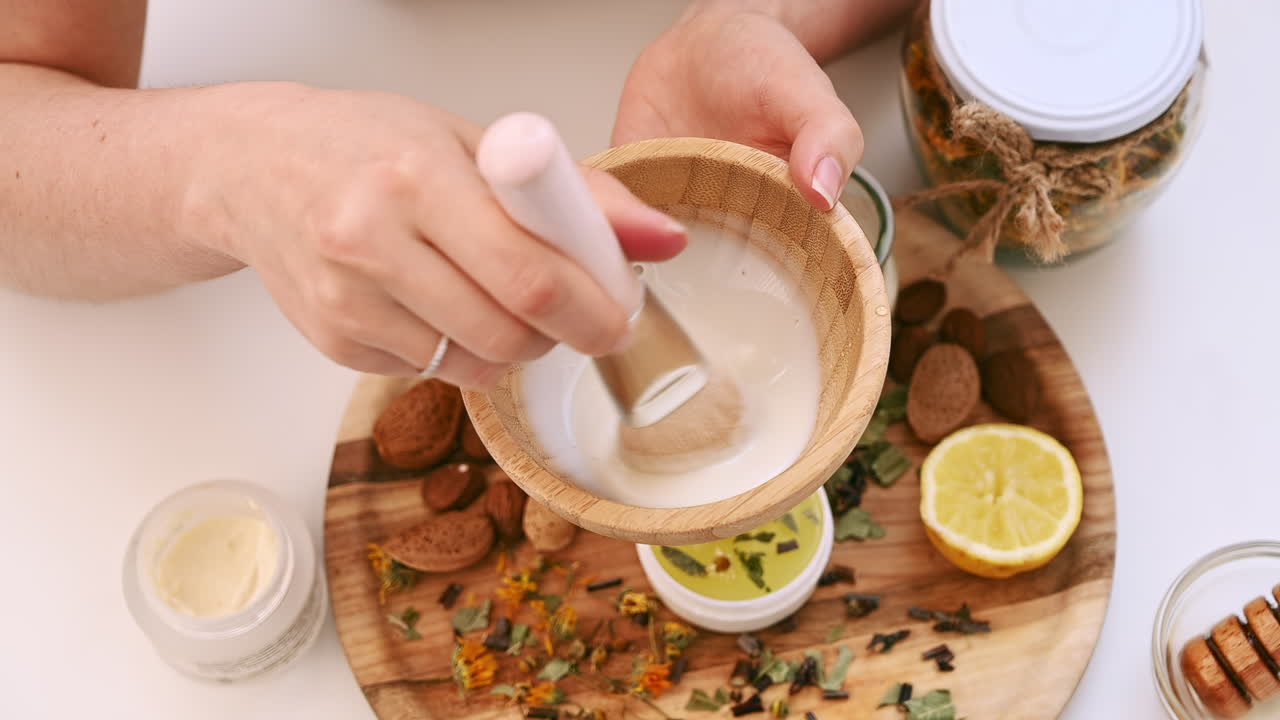 Hands mixing ingredients for a homemade beauty mask using honey, lemon, almonds, and herbs