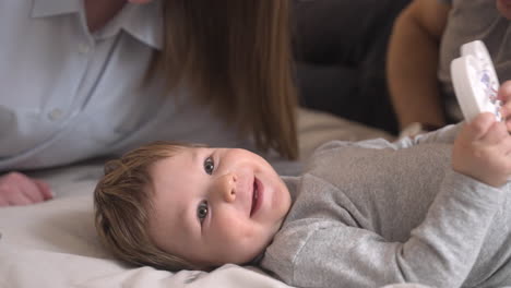 close up view of a baby looking at camera and lying on the bed playing with a toy heart while her mother kissing him