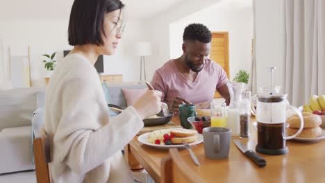 Happy-diverse-couple-sitting-at-table-and-having-breakfast