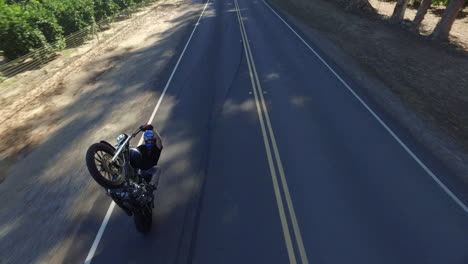 aerial over a motorcycle stuntman doing an outrageous wheelie on a california road