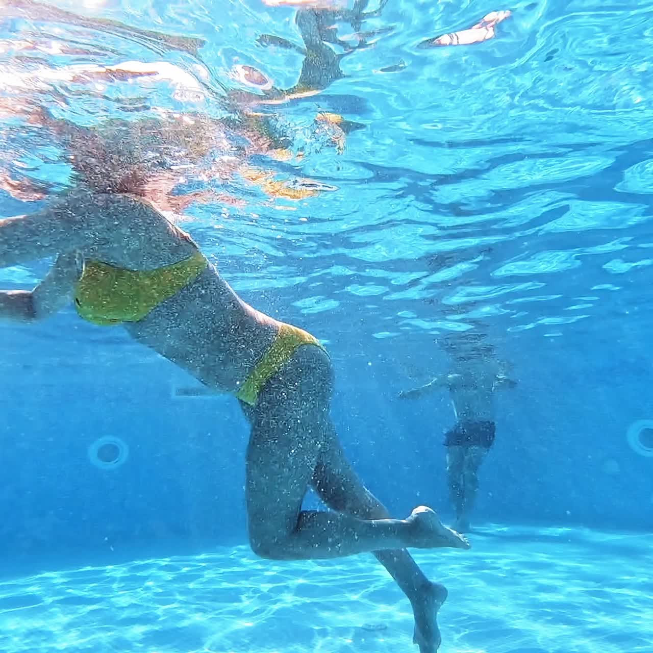 Underwater view of a young woman in a swimming pool. Woman in yellow swimsuit is swimming in the pool in summer.