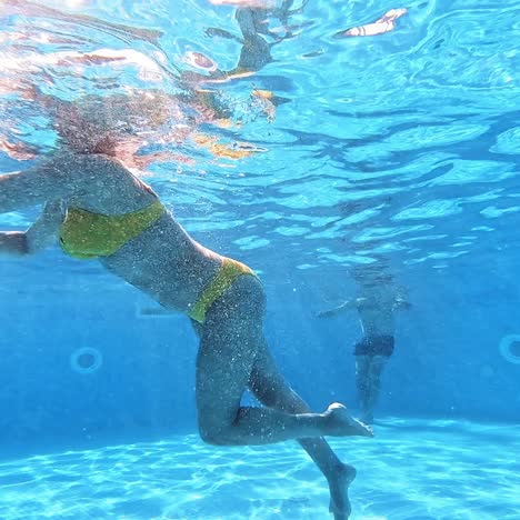 underwater view of a young woman in a swimming pool. woman in yellow swimsuit is swimming in the pool in summer.