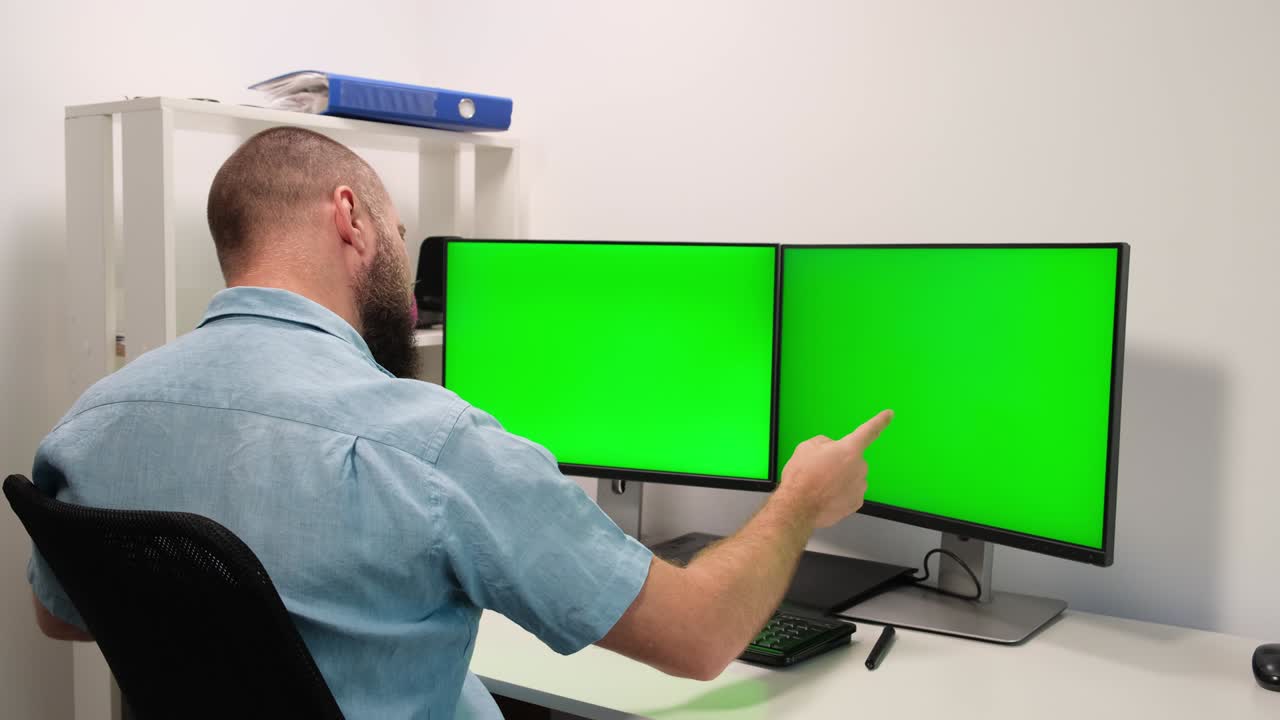 a man working at home in front of two green monitors. the man is happy with the result. remote work.