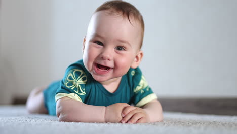 adorable smiling kid lies on the floor looking at camera. cheerful kid banging hands by the floor actively. close up.