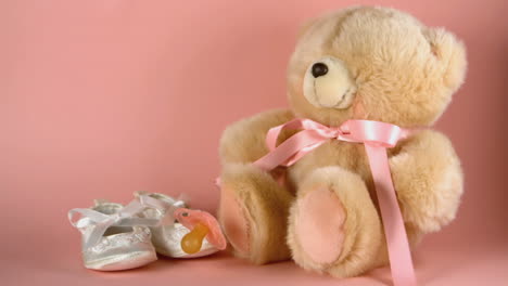 Pink-soother-falling-onto-a-teddy-bear-and-baby-shoes