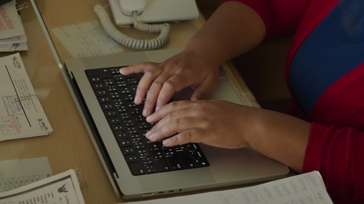 Primo piano delle mani di una donna d'affari che digita una ricerca sulla tastiera del laptop e ha redatto un rapporto aziendale sulla scrivania dell'ufficio di notte