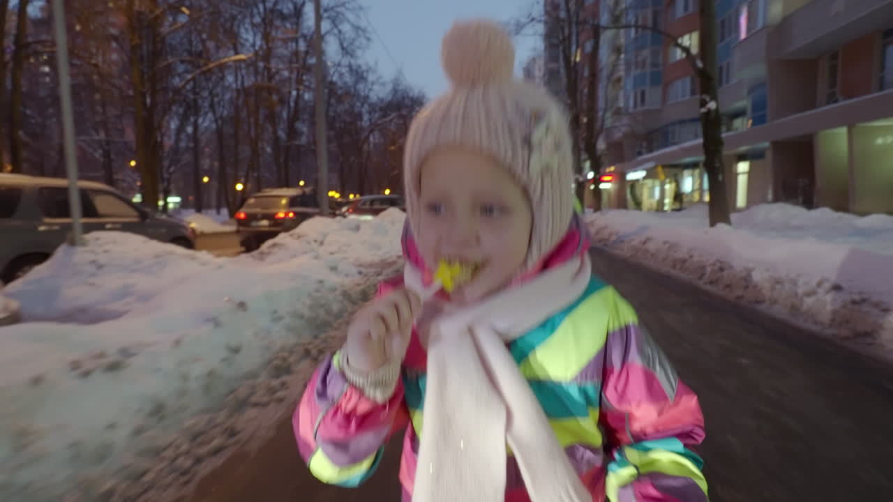 Iloinen lapsi juoksee talvisessa kaupungissa hämärässä.