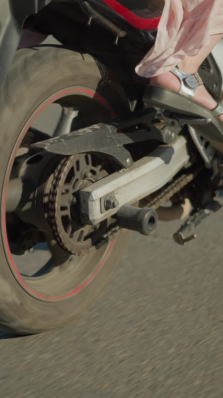 vista de las piernas de dos damas montando una bicicleta eléctrica mientras el viento agita su ropa, sus sombras se proyectan en la carretera mientras la bicicleta se mueve