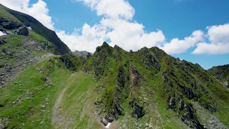 Vista-Aérea-De-Un-Hermoso-Paisaje-Montañoso-Con-Picos-Altos,-Nubes-Gruesas-Y-Esponjosas-Y-Un-Hermoso-Valle-Verde,-Montañas-De-Los-Cárpatos,-Carretera-Transfagarasan-Transilvania,-Rumania