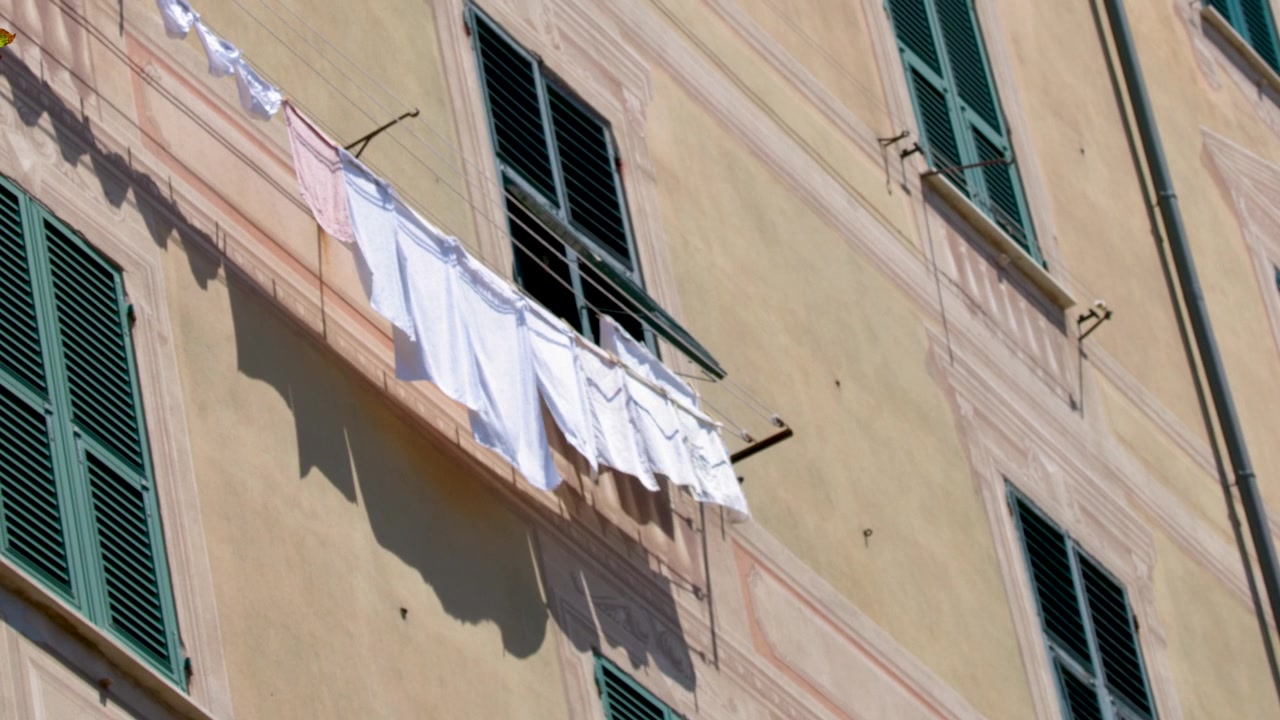Plano de baixo ângulo de roupa branca secando em um varal do lado de fora de um edifício de apartamentos mediterrâneo.