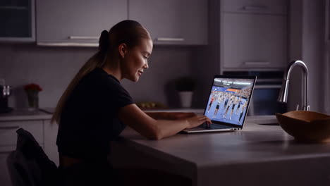 woman watching sports on laptop in kitchen