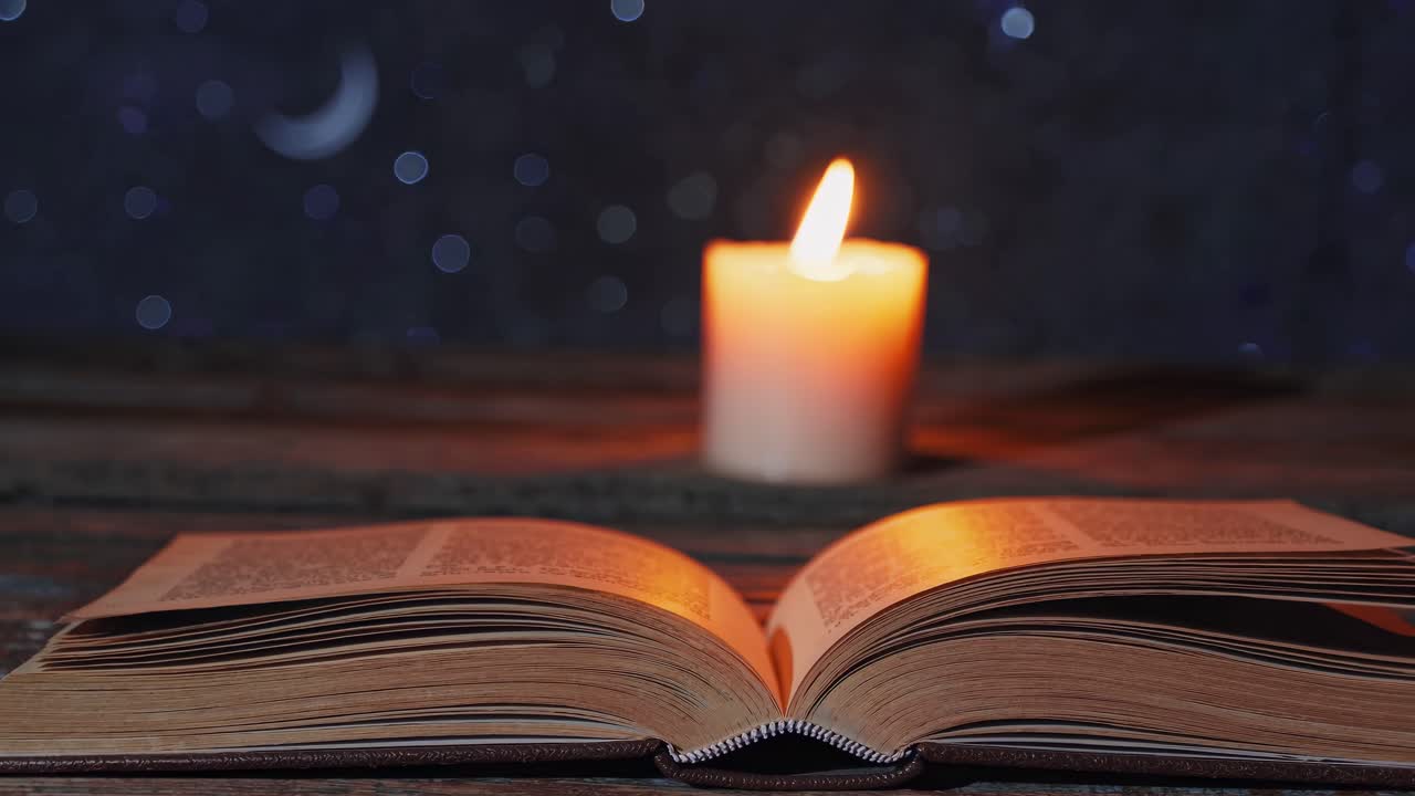 A close-up video of an open book with pages turning, illuminated by candlelight