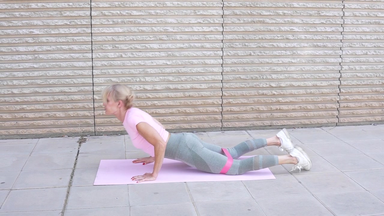 A woman is engaged in a stretching and exercise regimen outdoors while using a yoga mat