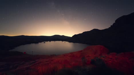 night timelapse of the milky way and stars above laguna grande de peñalara in sierra de guadarrama, with light pollution on the horizon