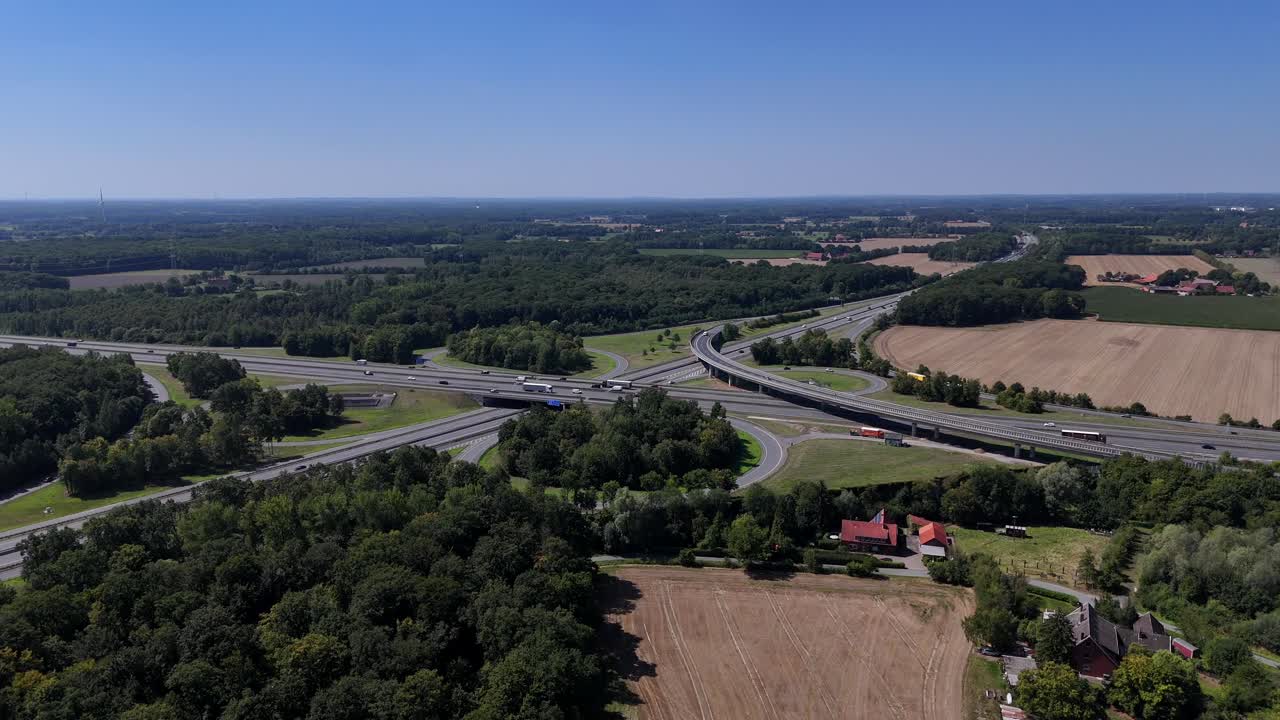 Aerial rising establishing shot of German autobahn motorway junction and historic rustic farm steads. Wide shot. Sunny summer day with blue sky. Rural suburb with cropland. Driving cars on new road
