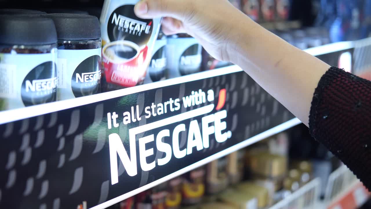 persona recogiendo un frasco de nescafe en una tienda de comestibles