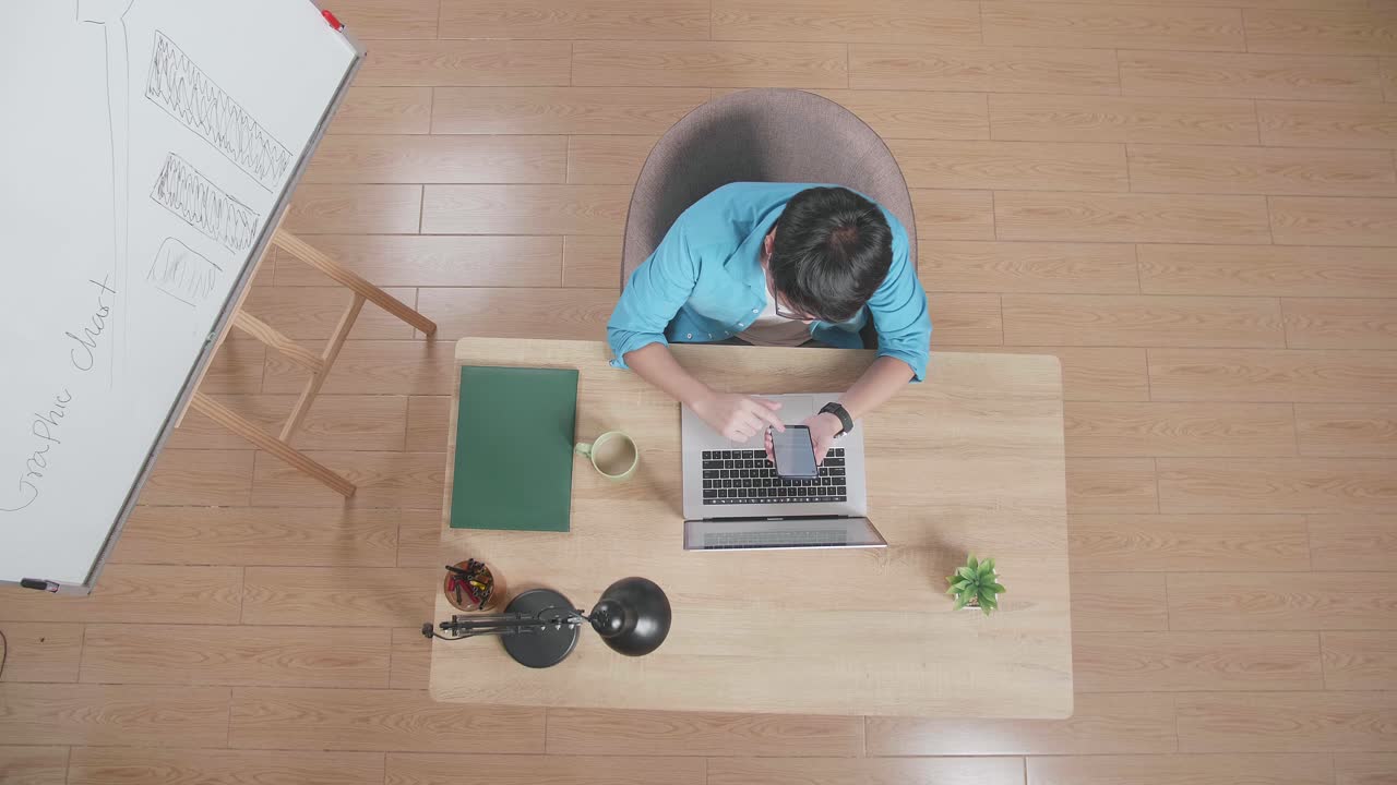 위쪽 뷰에서  아웃 으로 스마트폰을 사용하는 남자가 집에 있는 노트북에서 화이트보드 에 앉아 있는 모습