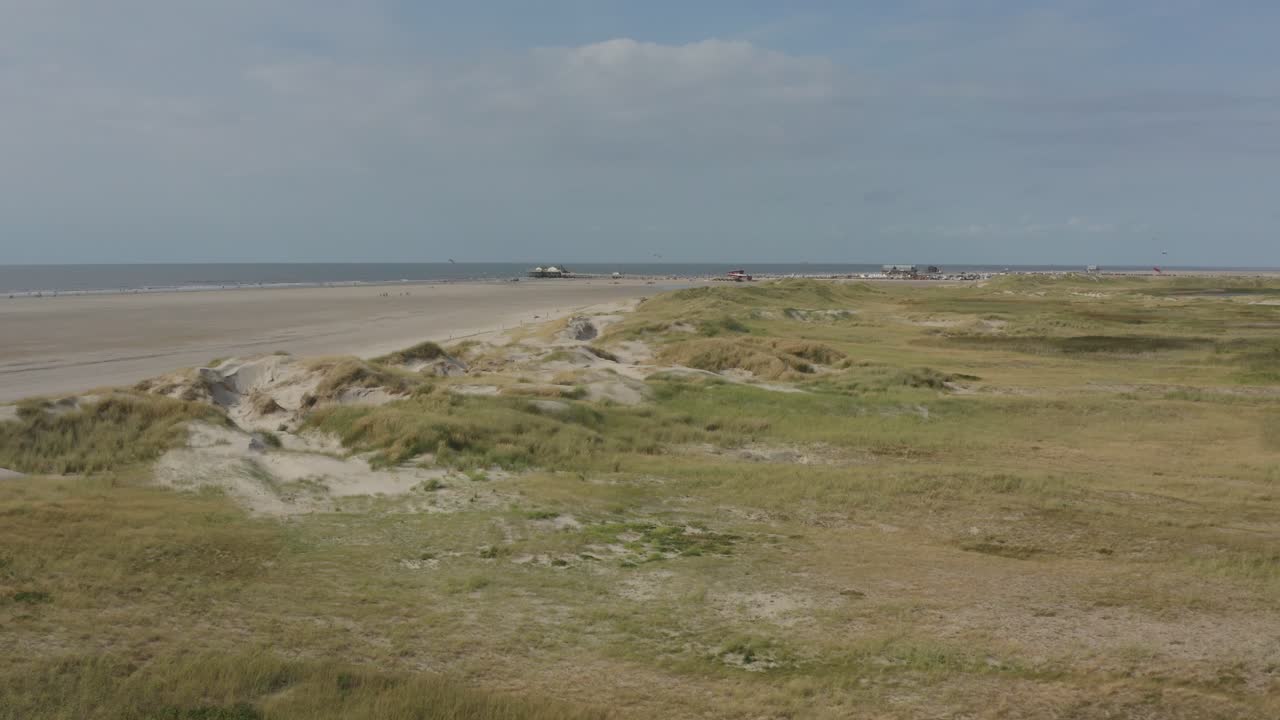 Filmisk drönar- / flygbild av den gröna och sandiga naturstranden i St. Peter Ording vid Nordsjön med kitebuggy, Schleswig-Holstein, Tyskland, 30p