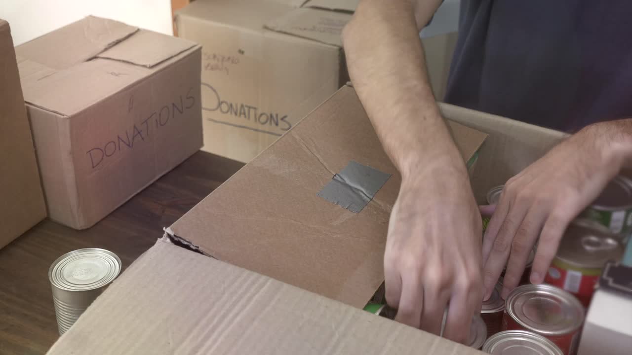 Hænder pakker dåsevarer i en papkasse til donation