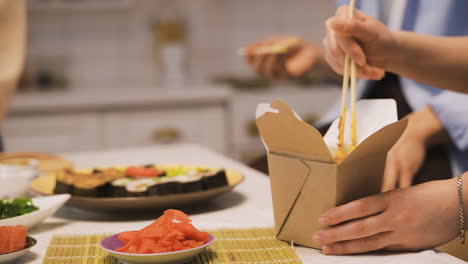 vista ravvicinata delle mani di una donna che tengono le bacchette e raccolgono ramen da asporto