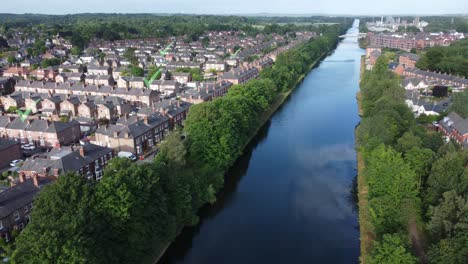 Green-tick-icon-flashing-above-sunny-British-homes-alongside-long-canal,-Rising-aerial-view