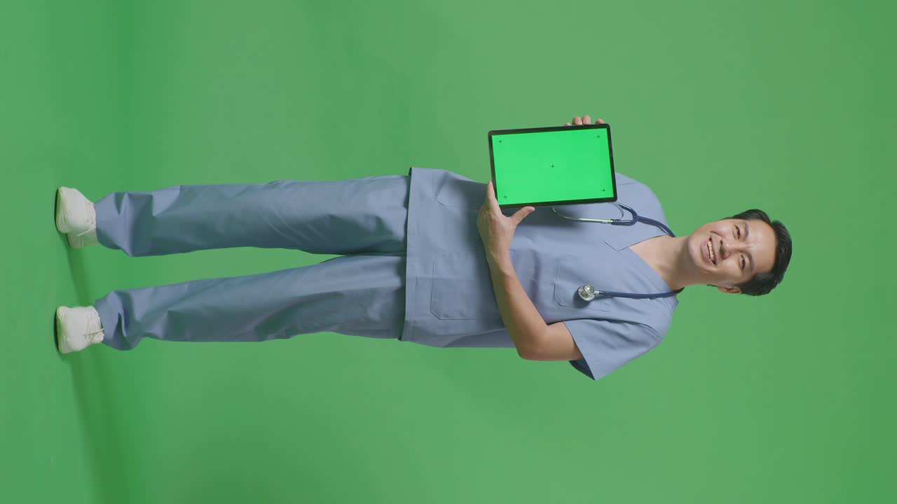 cuerpo lleno de médico masculino asiático con estetoscopio sonriendo y mostrando tableta de pantalla verde mientras está de pie en el fondo de la pantalla verde en el hospital