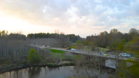 gorgeous aerial drone footage rising up and flying higher in front of a rural dark colored river with golden sunset reflections on it while kayakers are paddling on the river during a marathon.