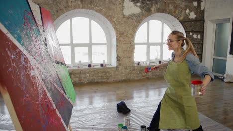 female artist emotionally creates masterpiece of abstract painting in studio, side view