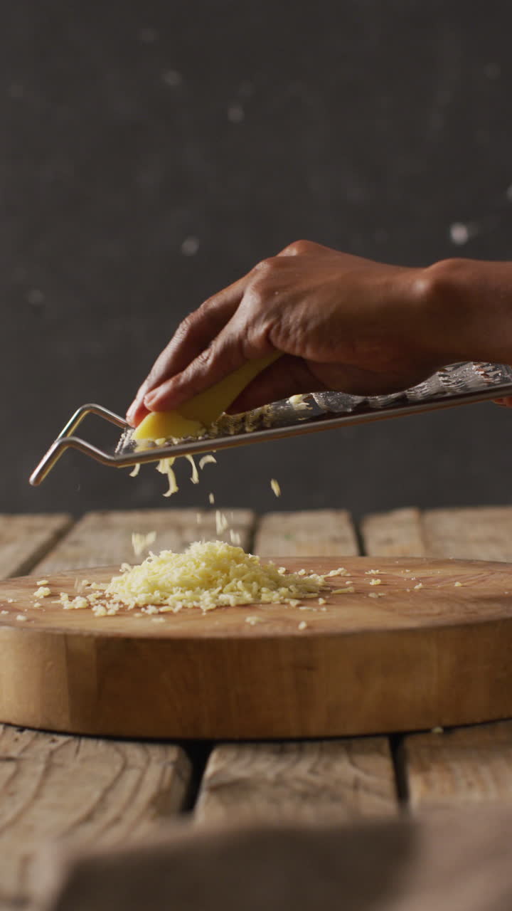 Video verticale di uomo birazziale che grattugia formaggio con una grattugia su un tagliere di legno