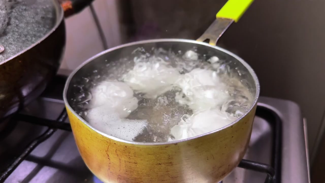 Close up of white eggs boiling in hot bubbling water inside a yellow pot on a kitchen gas stove. Professional culinary footage for healthy breakfast and meal preparation lifestyle content.